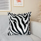 A cushion cover with a black and white zebra pattern, placed on a sofa in a living room setting.